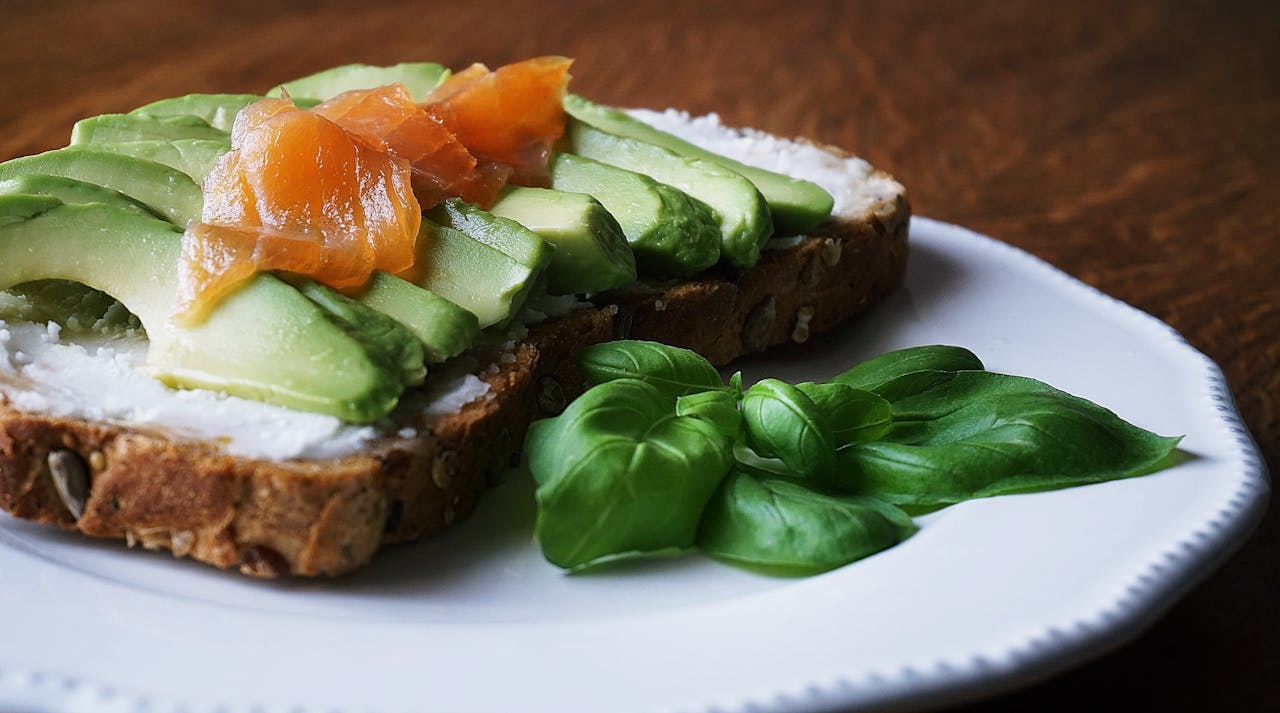 services-06 A delicious, healthy meal with avocado and smoked salmon on seeded bread, garnished with basil leaves.